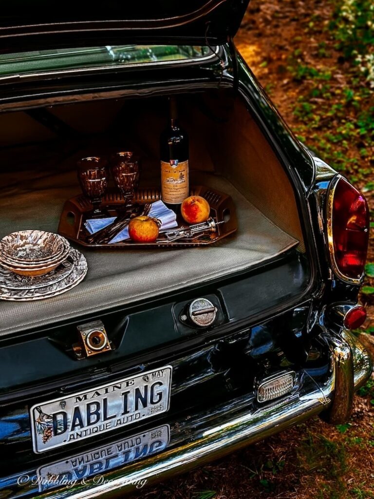 Open trunk of VW 1968 Fastback tray of wine, glasses and vintage dishes in a car picnic.