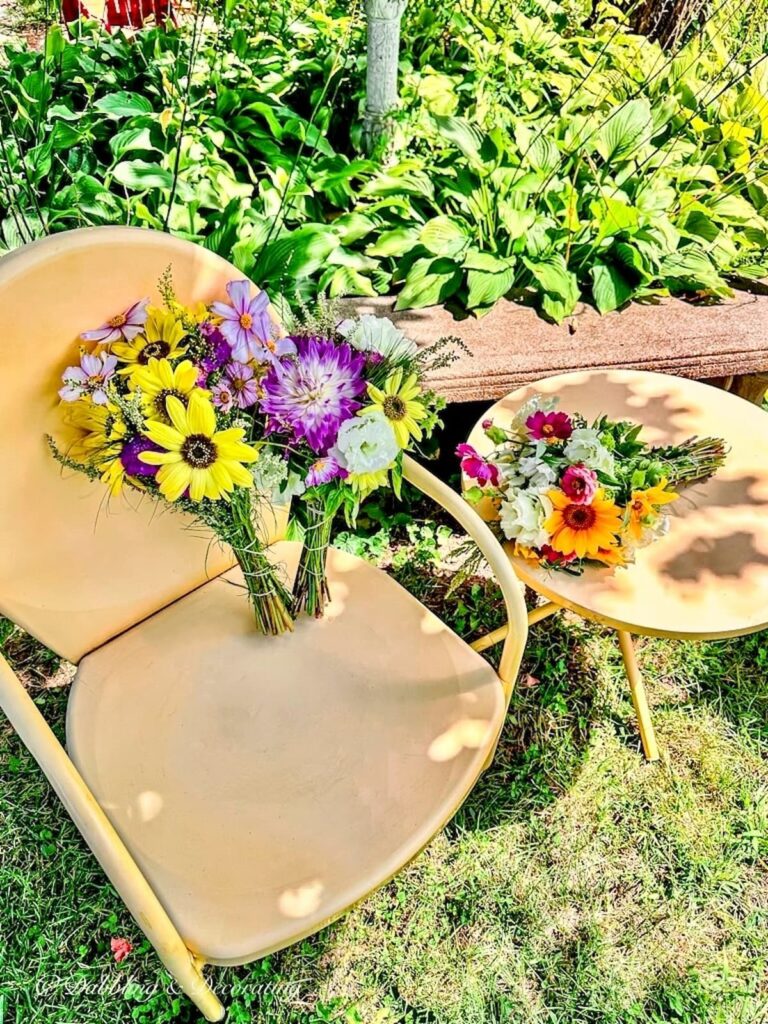 Bouquets of wildflowers in vintage yellow wrought iron chair and table outdoors.