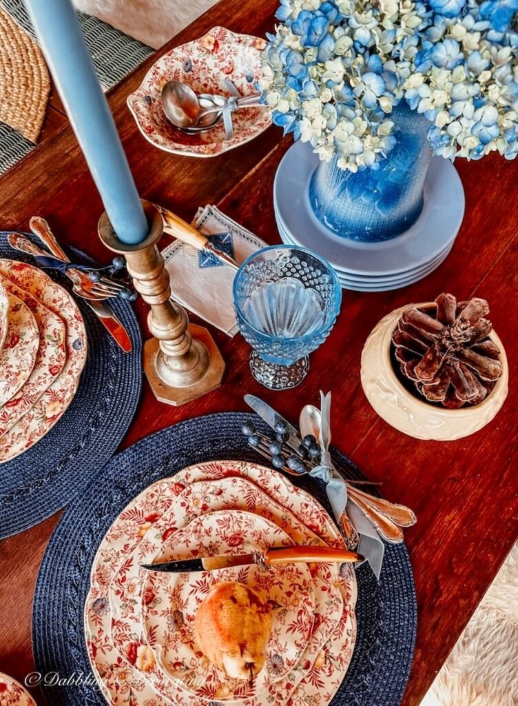 Brass candlestick with blue taper candle and vintage dinnerware on fall tablescape.