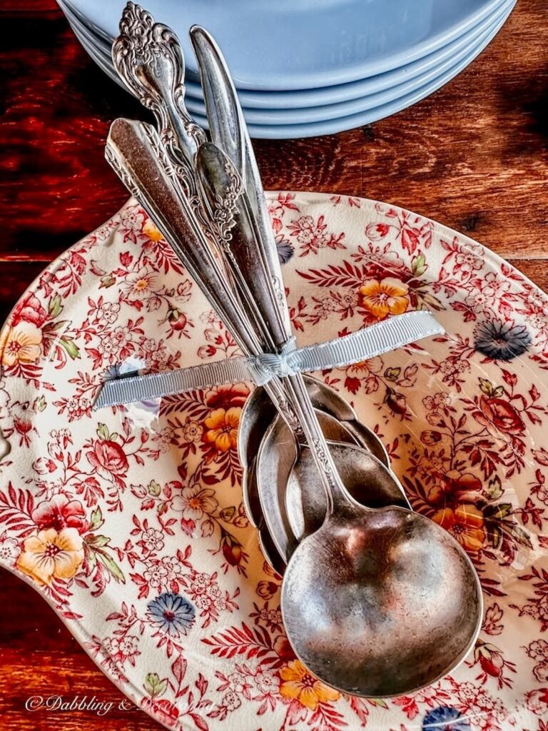 Vintage Johnson Brothers bowl with vintage silver serving spoons tied in blue ribbon next to blue plates.