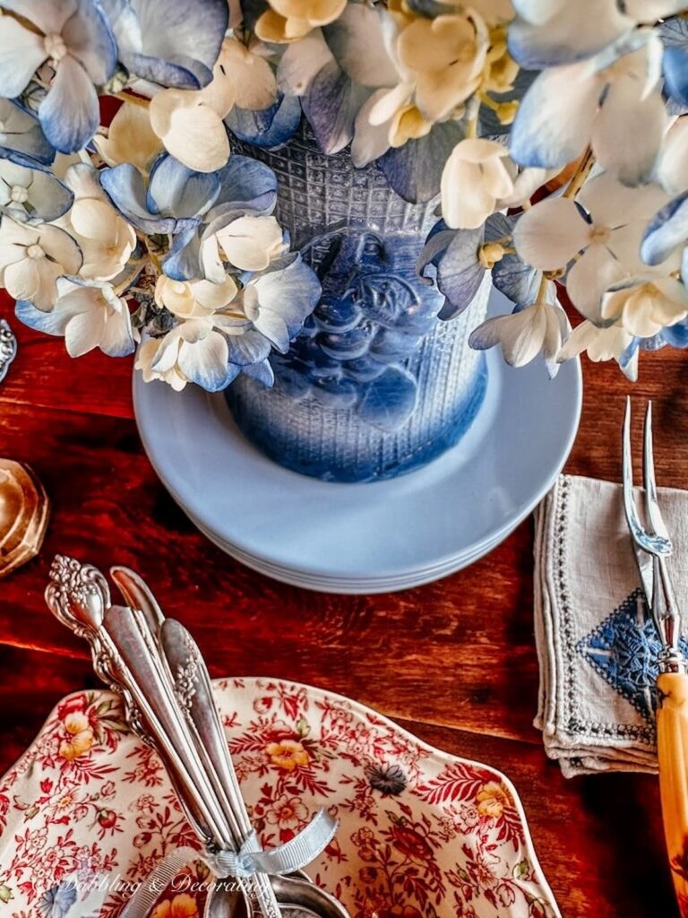 Vintage blue stoneware vase with blue hydrangeas on blue dishes on fall tablescape.