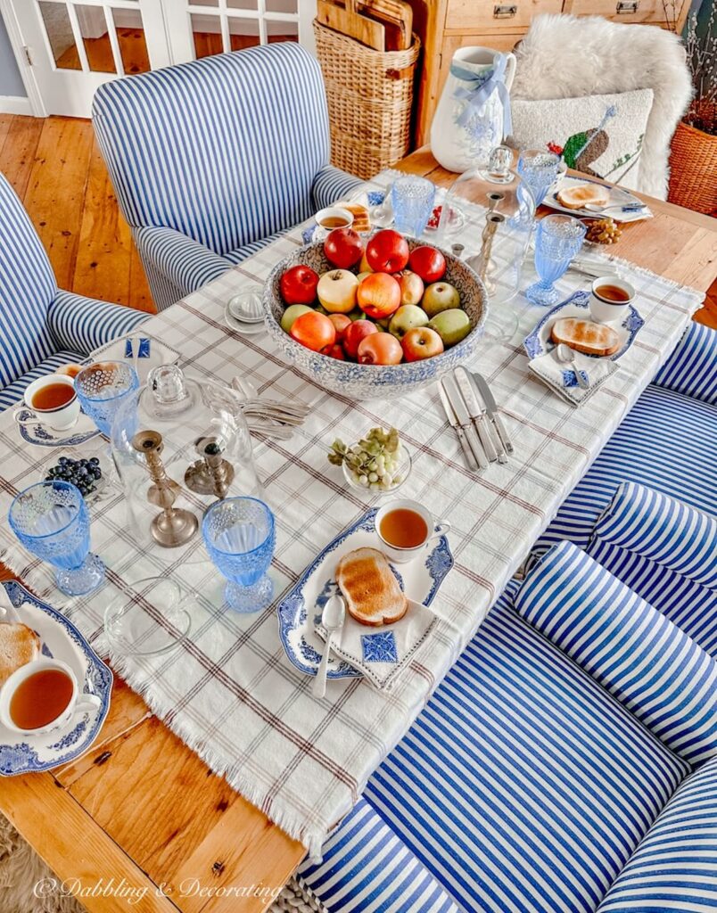 Blue and white styled fall tablescape with bowl of red apples as centerpiece.