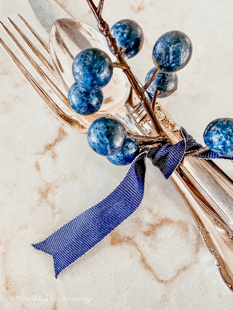 Silverware place setting tied together with a blue ribbon and a blueberry branch.