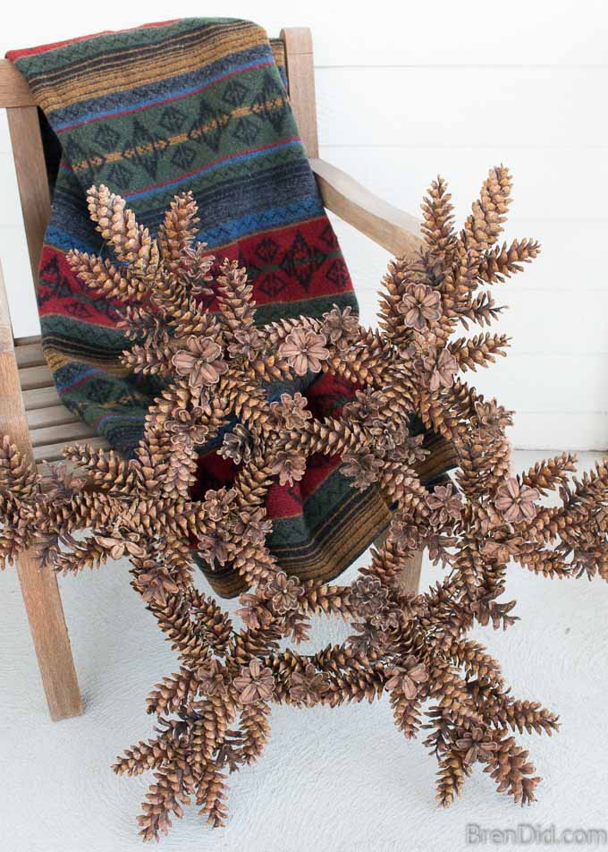 Pinecone snowflake wreath next to winter blanket on white porch.