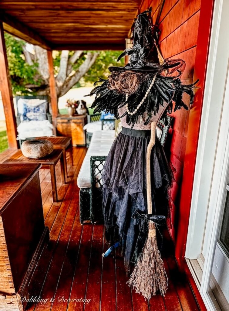 Witchy decor on Mannequin on front porch of red home.