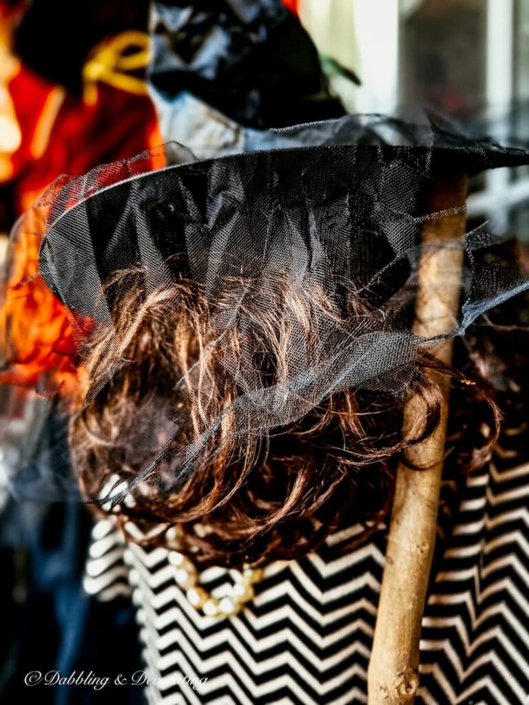 Brunette wig with witch hat and veil on mannequin for Halloween with witches broom.