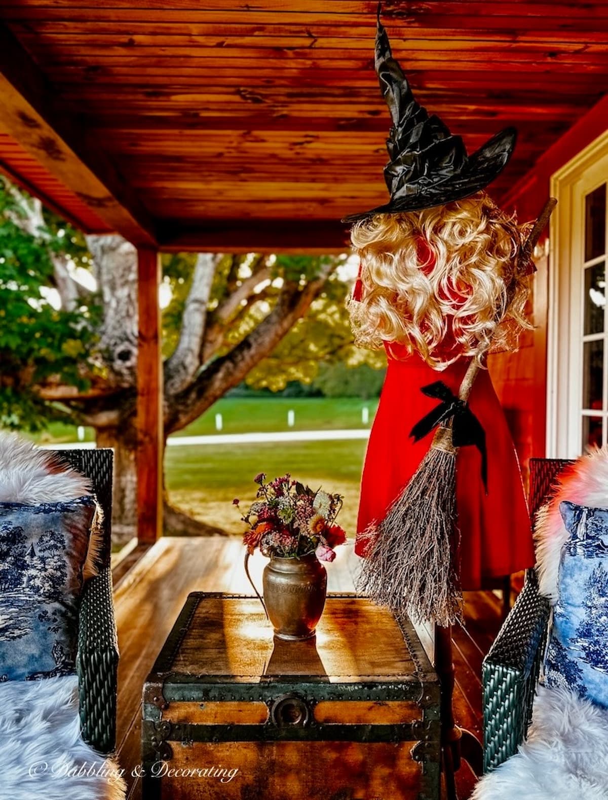 Mannequin dressed with red dress, witches hat, witches broom on wooden style porch for Halloween.