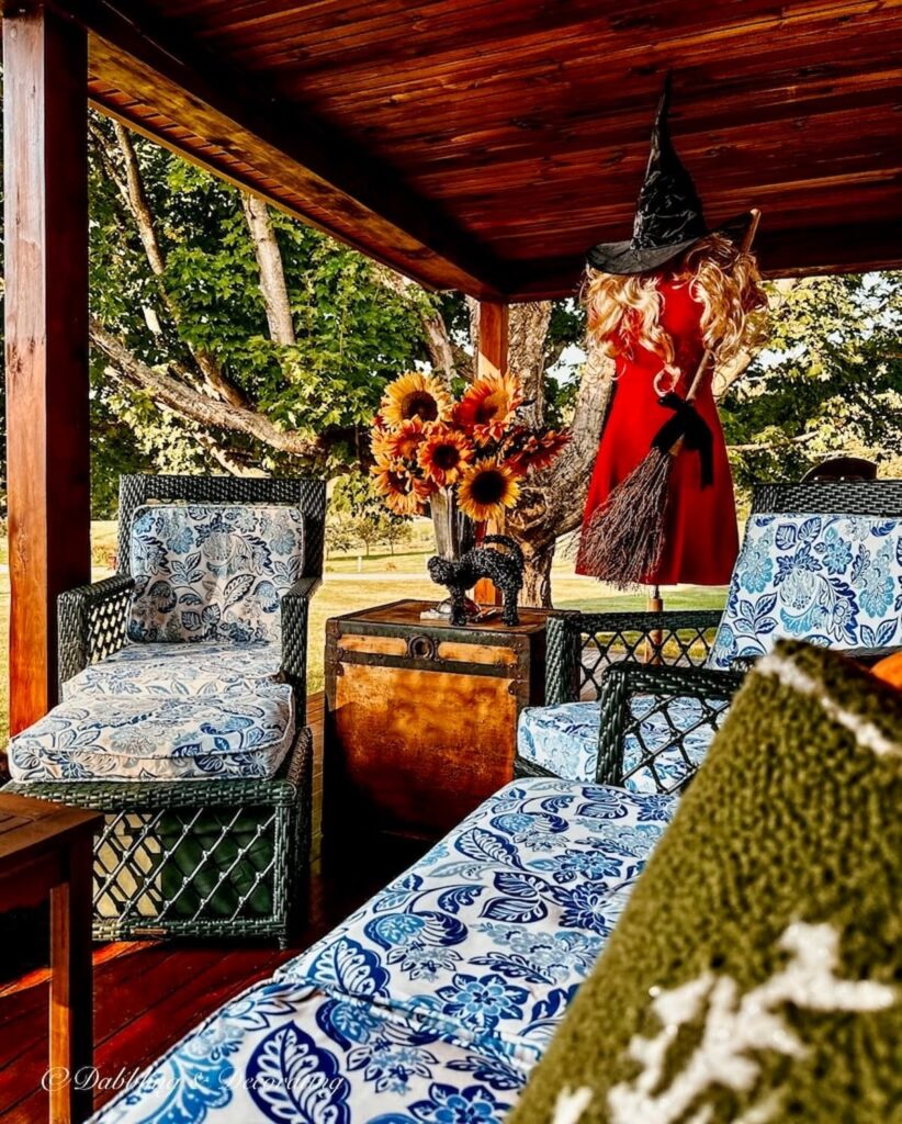 Mannequin dressed in witchy decor on front porch with blue cushions and sunflower bouquet for fall.