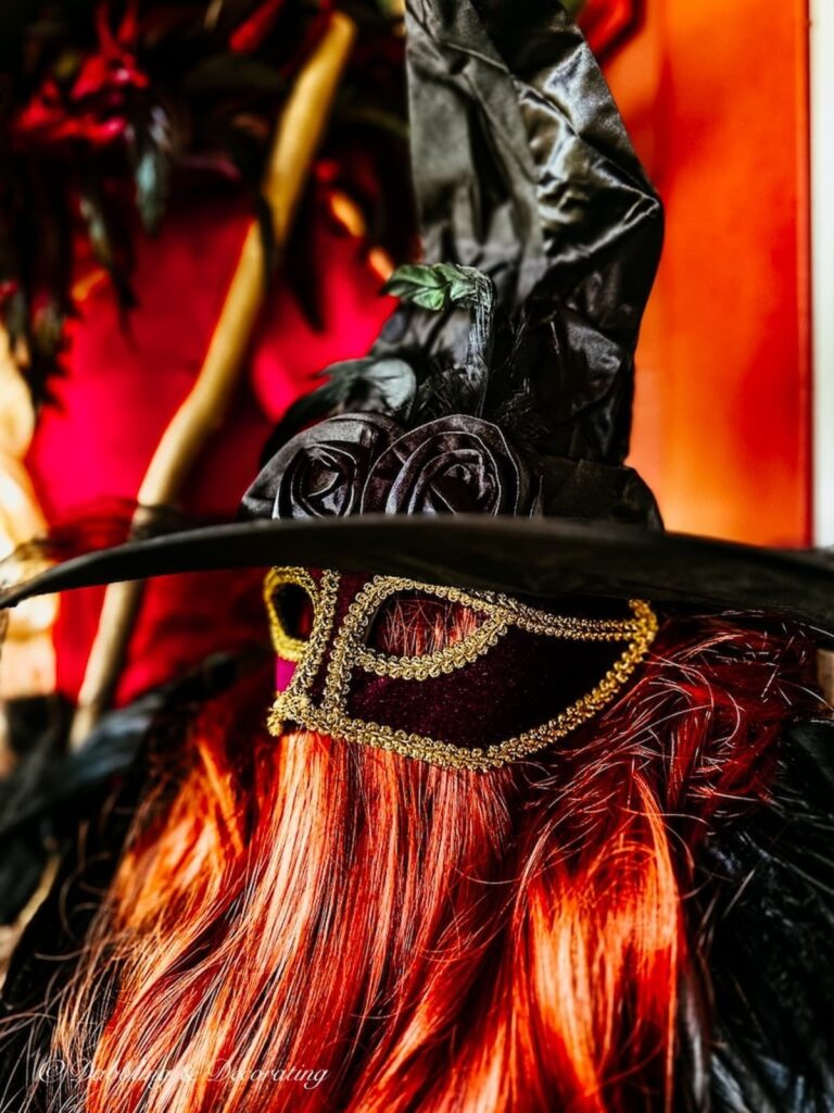 Witchy decor with red wig, masquerade mask, black witchy hat on mannequin for Halloween.