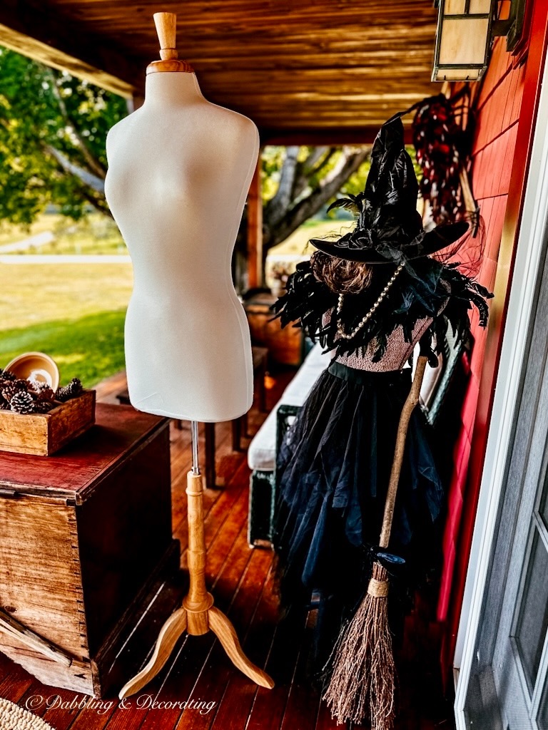 Two mannequins one is dressed with witchy decor on front porch.