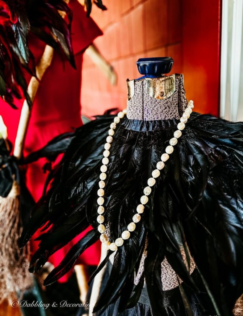 Witchy decor with black feather shall and string of pearls on mannequin for Halloween.