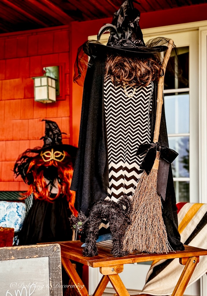 Mannequin witchy decor with broom, hat, and black cat with cape and red head witch behind it on front porch.