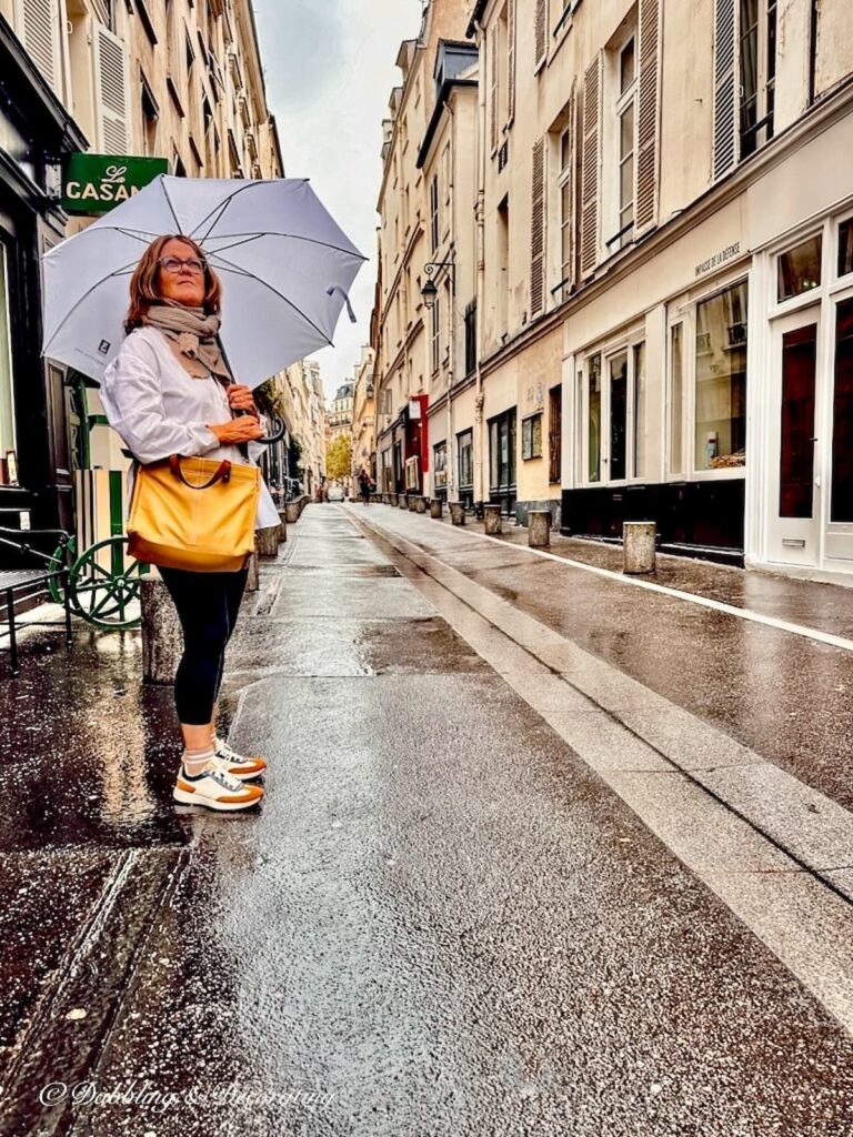 Woman standing with umbrella with yellow bag on the streets of Paris looking up to the sky.