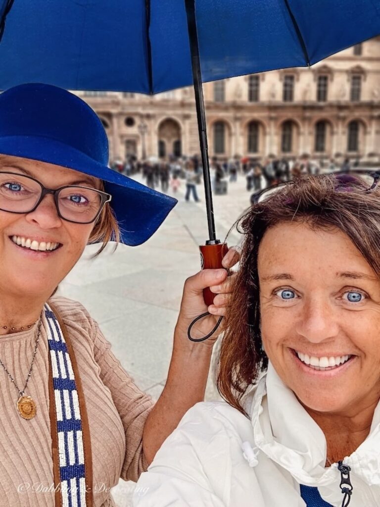 Two women under a blue umbrella in Paris on a rainy day.