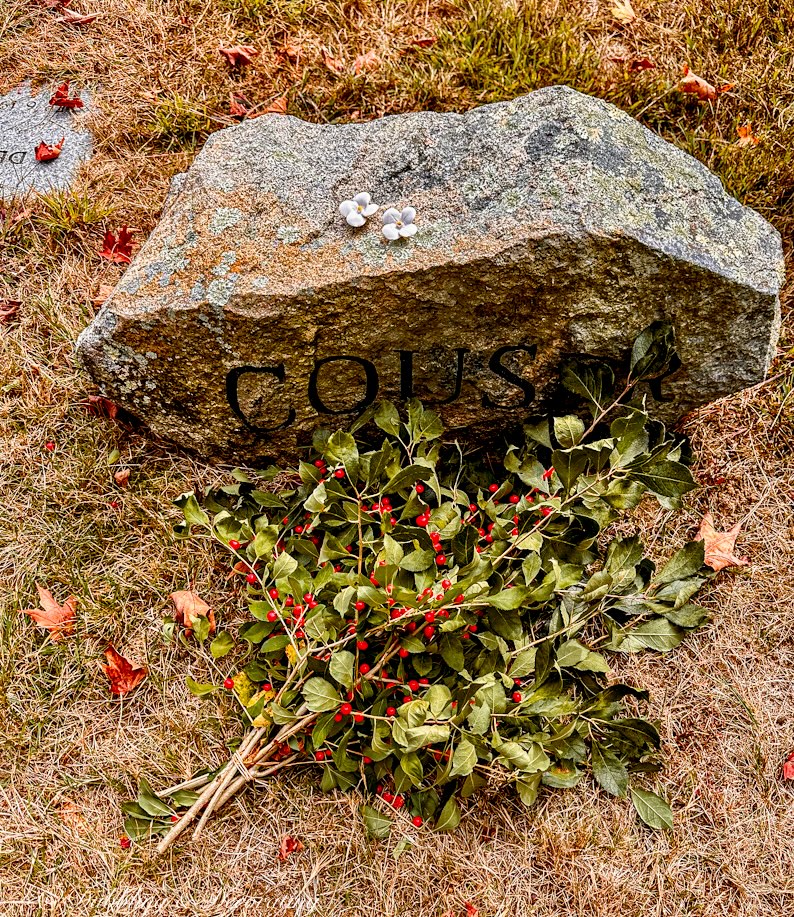 Cemetery stone rock with two white immortelles flowers on top with resting bouquet of winterberries.