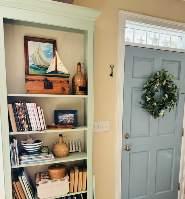 Blue inside door with wreath and coastal styled bookshelves with vintage demijohns.