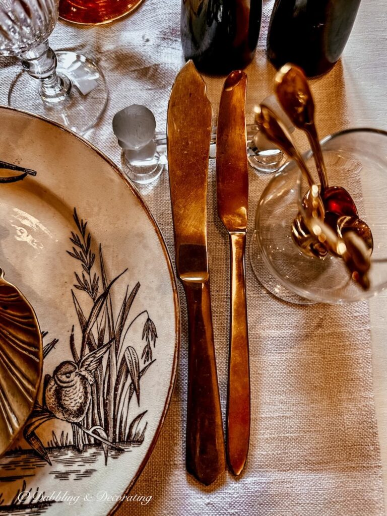 Gold flatware on brown table setting with knife rest in France.