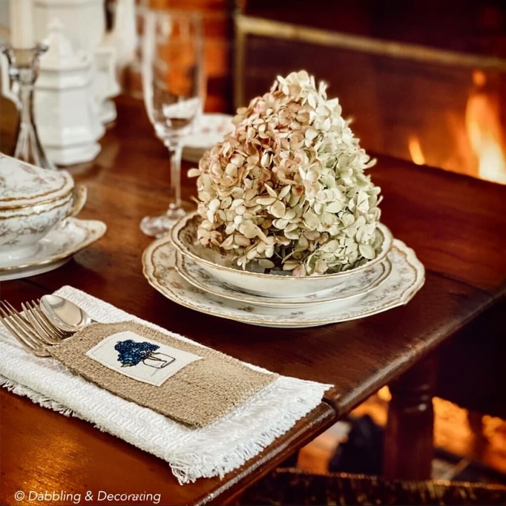 Fall hydrangea on vintage place setting in front of fire in the fireplace.