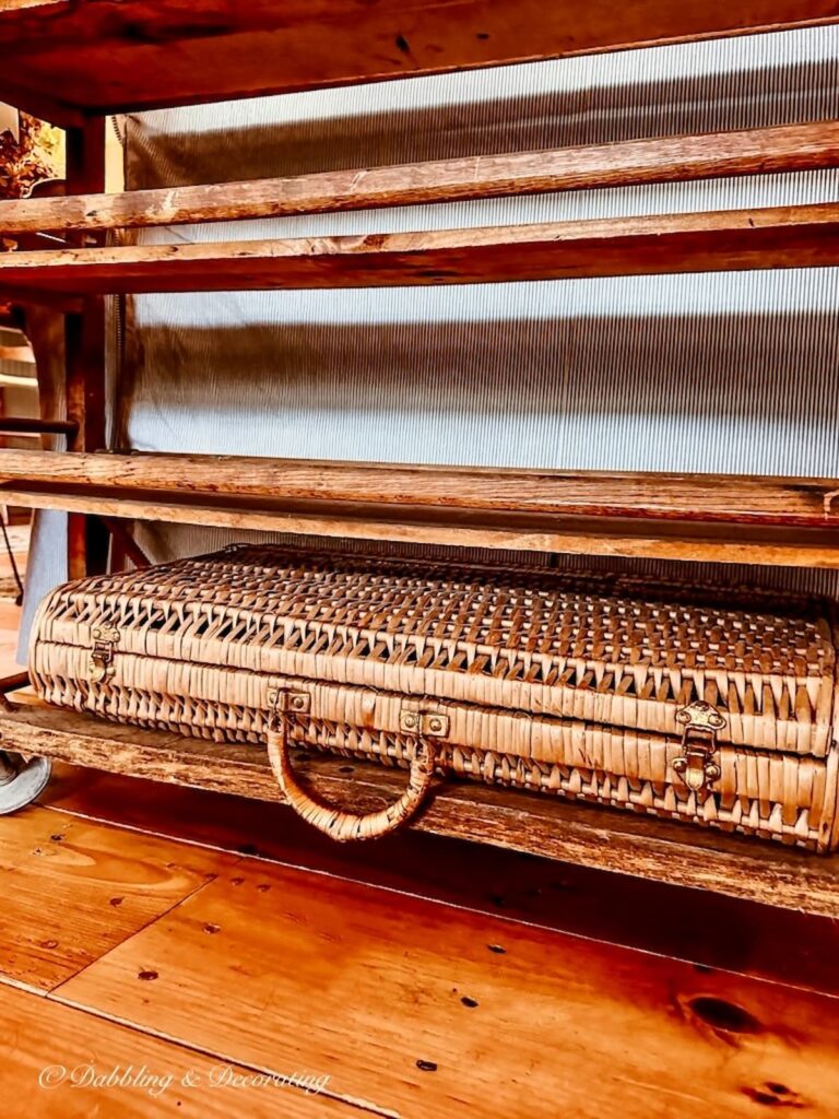 Wicker suitcase on bottom shelf of antique cobbler rack.