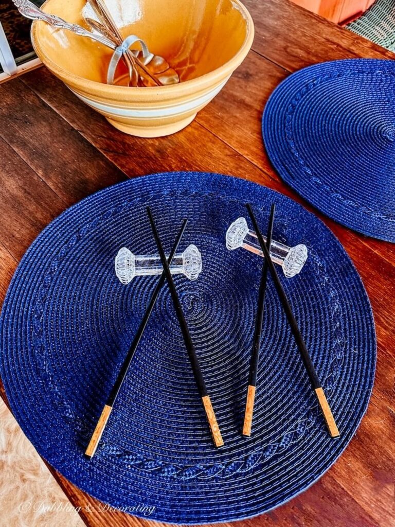 Chopsticks on antique crystal knife rests on blue placemat on table.