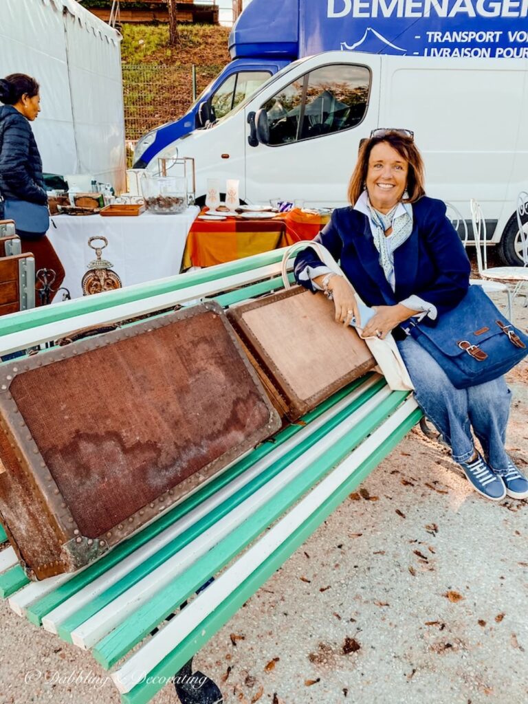 Woman sitting on a green and white bench with vintage suitcases at Paris flea market.