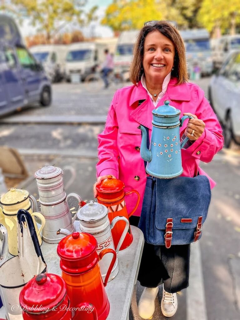 woman at street fair in pink coat holding up a blue antique pitcher.