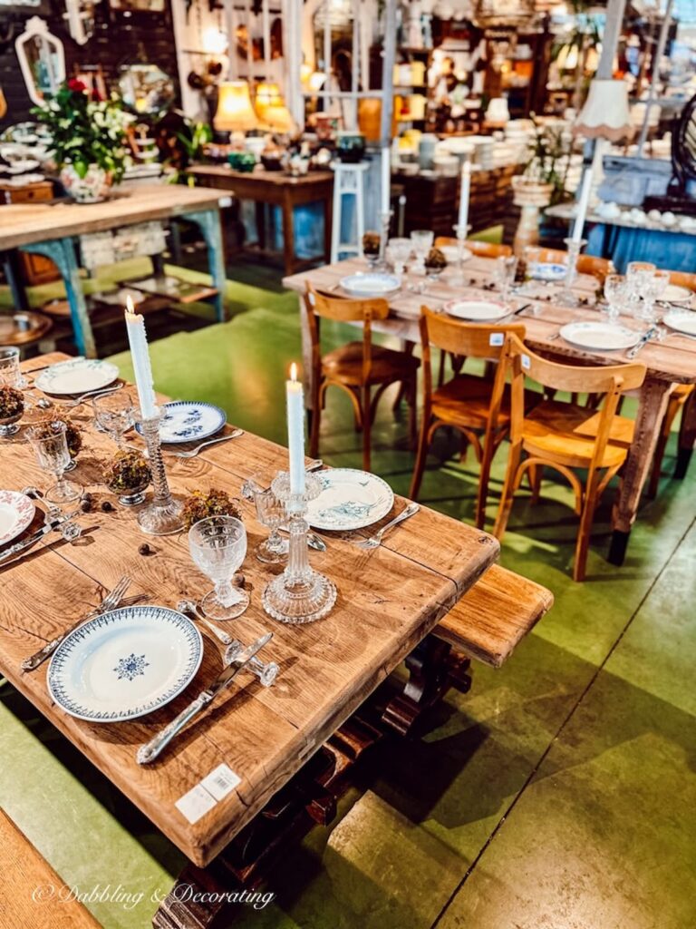 Two wooden antique tables set for lunch in a vintage shop warehouse.