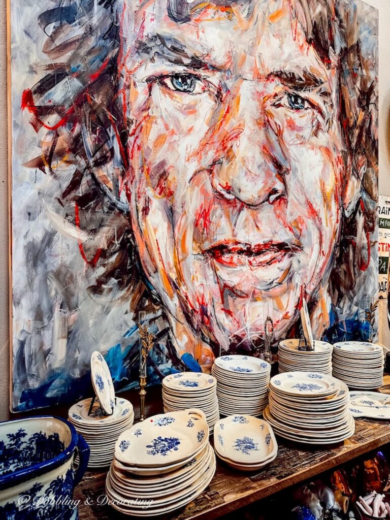 Large painting of man at Paris flea market with table of dishes.