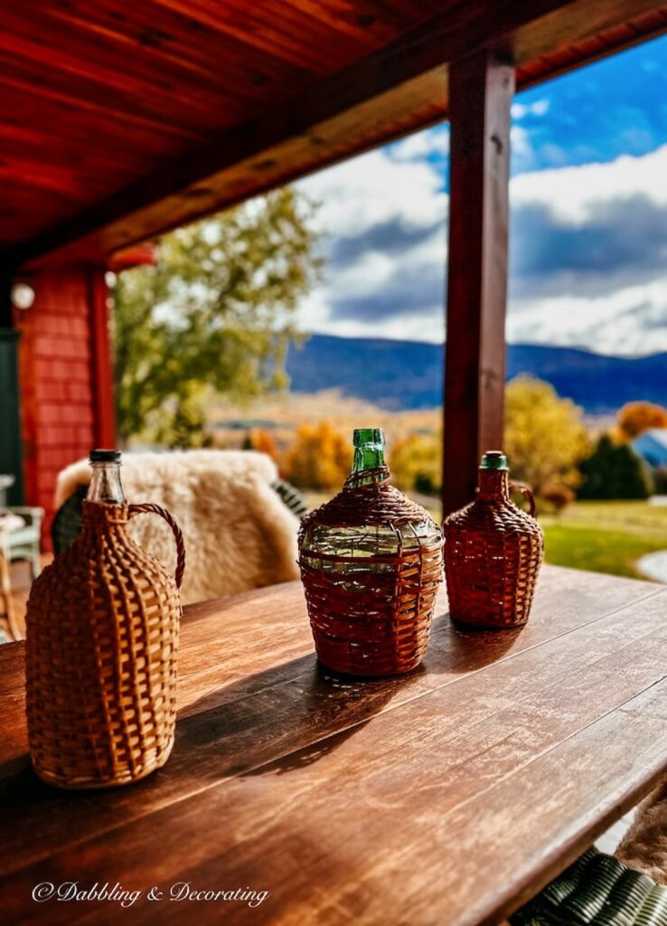 Three vintage demijohns on outdoor porch wooden table in the Vermont mountains during peak fall foliage.