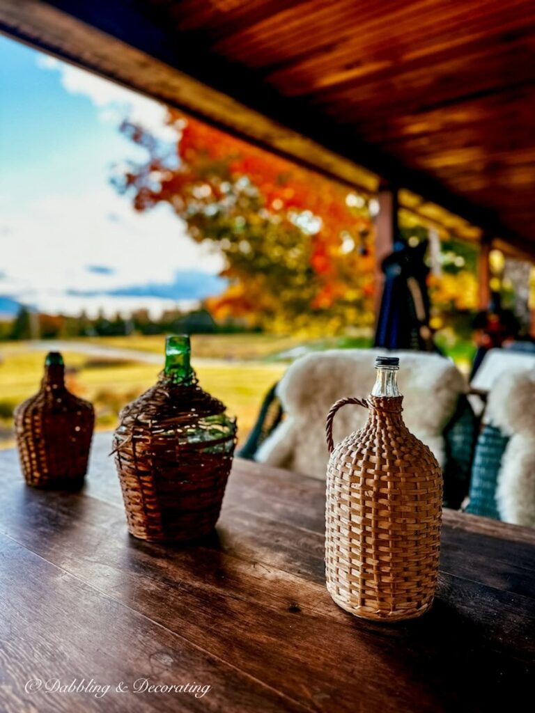 Three vintage demijohns on outdoor porch table with Vermont fall foliage views.