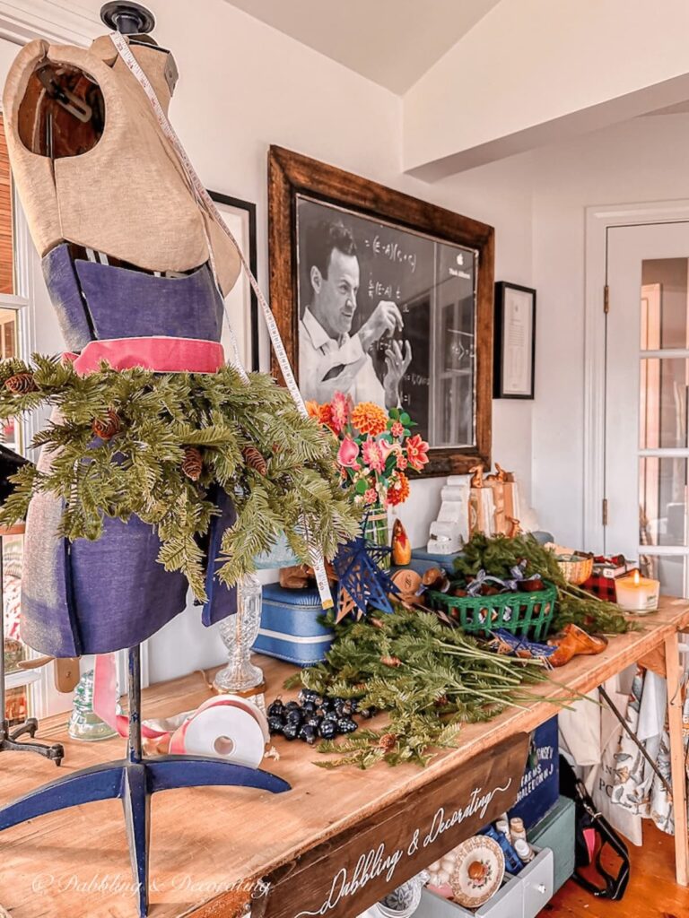 Craft table with mannequin and evergreens decorating for Christmas.