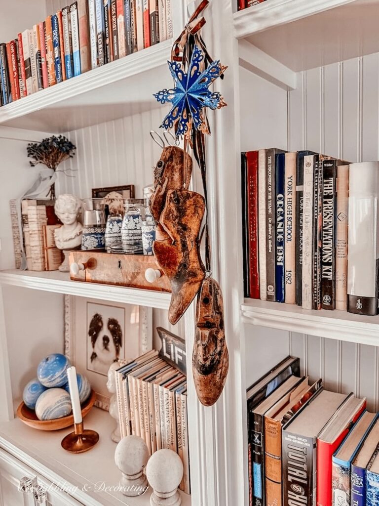 Vintage wooden cobbler shoe molds hanging from built-in bookshelves with blue snowflake and brown velvet ribbon.