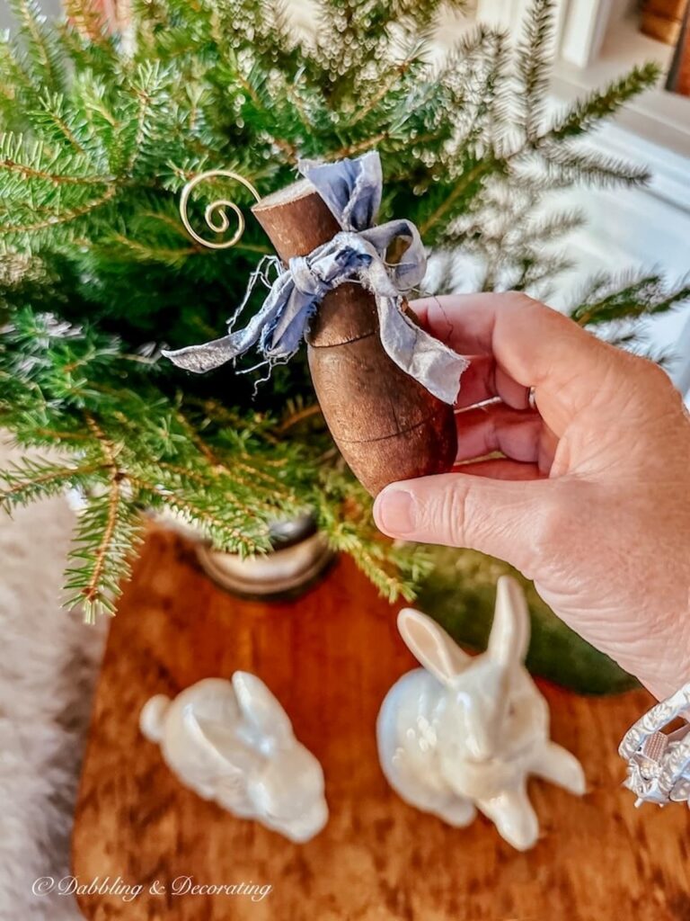 Decorative wood spindle with blue bow and Christmas tree hook in hand.