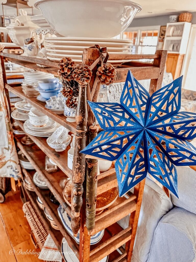 Navy blue star snowflake hanging on vintage cobbler rack with decorative wood spindles.