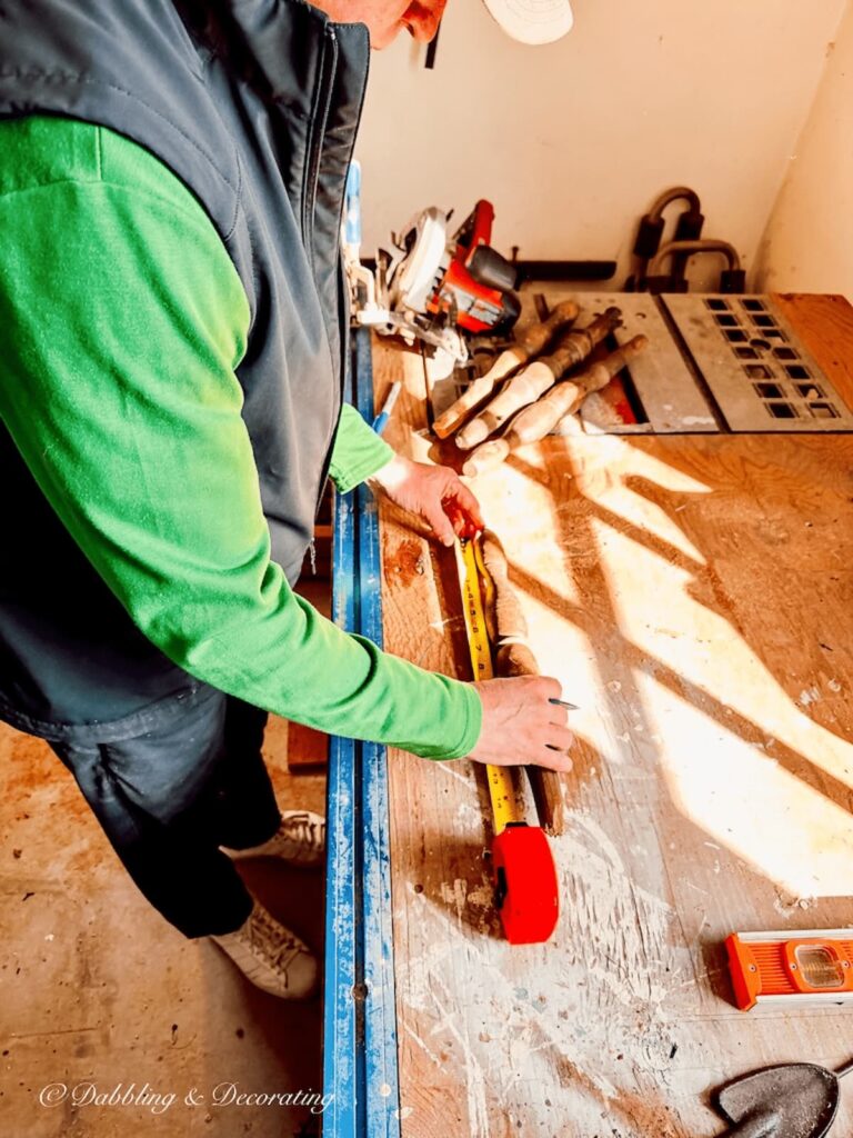 Man in green shirt measuring decorative wooden spindles on workbench.