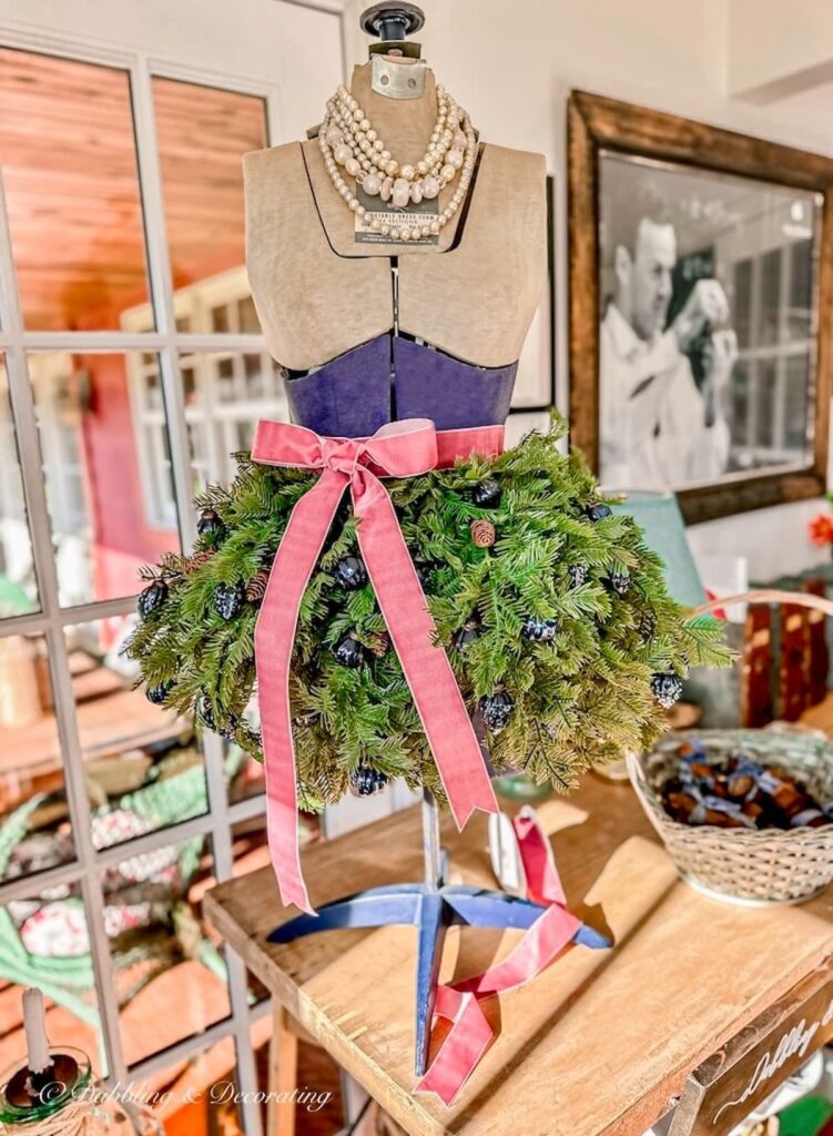 Christmas tabletop adjustable mannequin with evergreens, pink ribbon, navy blue vintage ornaments. 