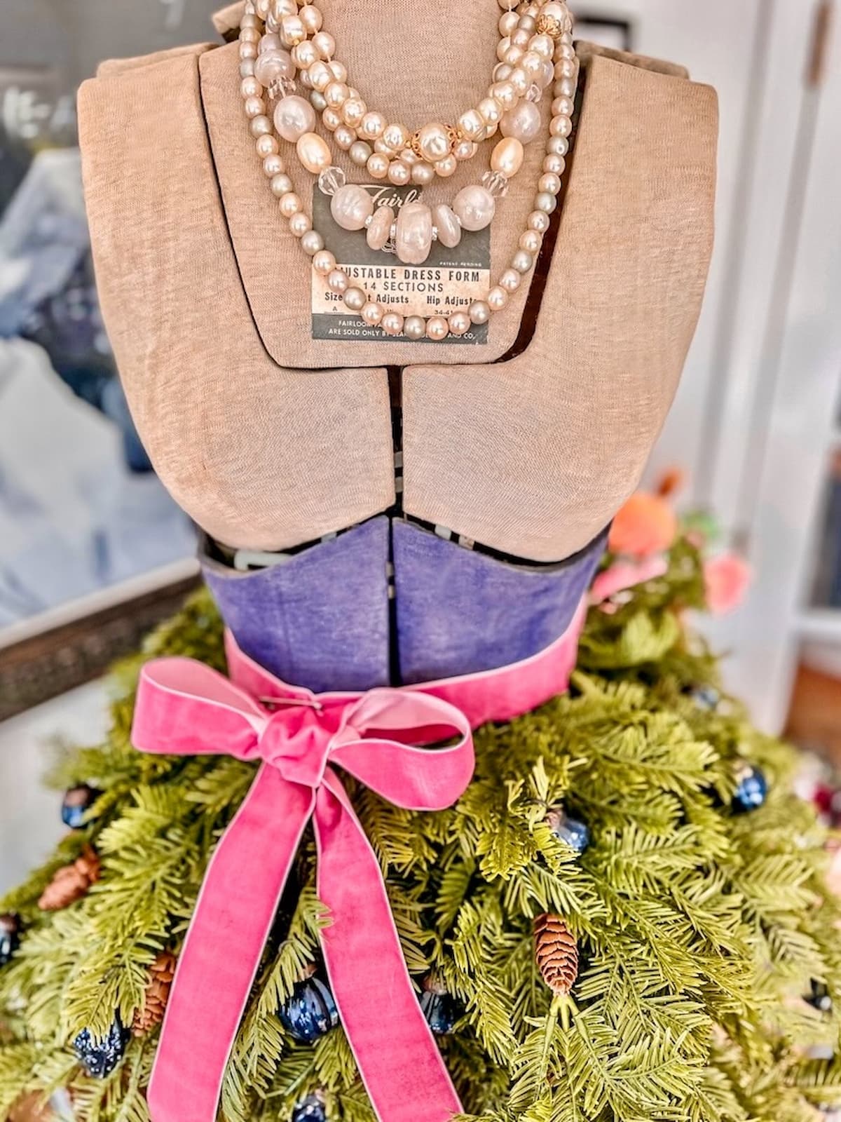 Vintage bust form decorated for Christmas with pink ribbon, evergreens, and string of pearls.