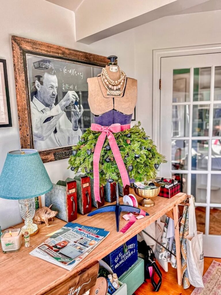 Vintage bust form decorated for Christmas with evergreens and a pink bow on vintage craft table.