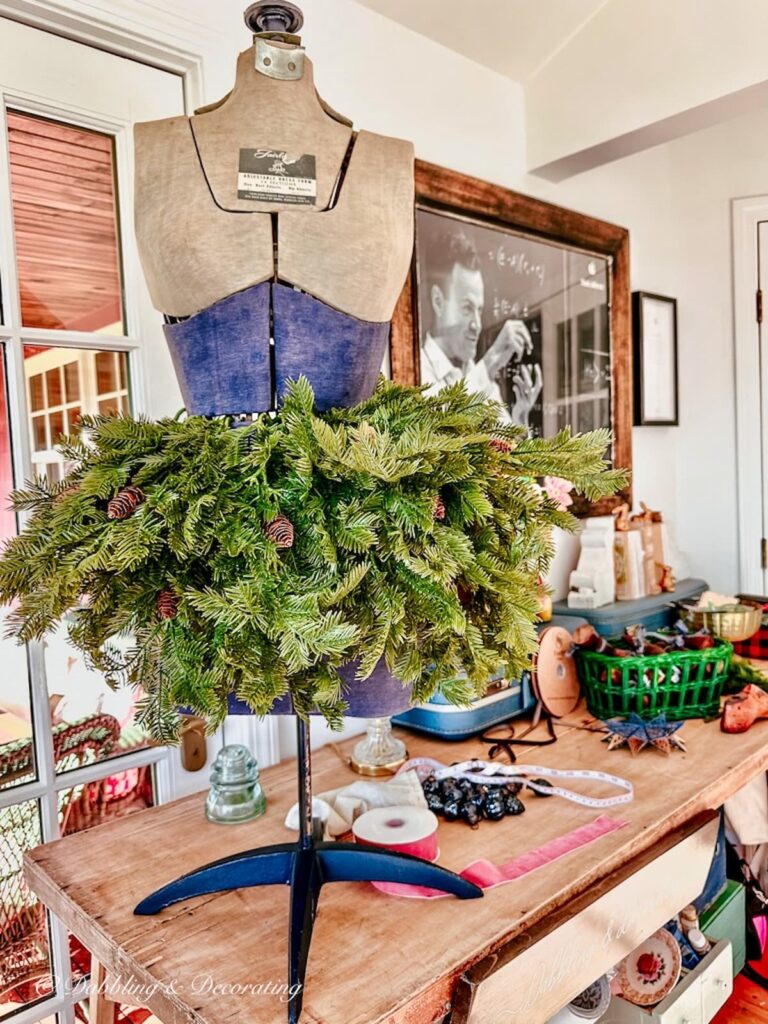 Vintage blue and gray bust form on table with faux evergreens around the waist for Christmas decor.