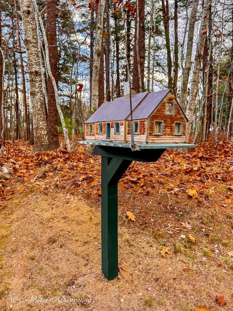 Cedar shakes mailbox on green post curbside in next to wooded trees.