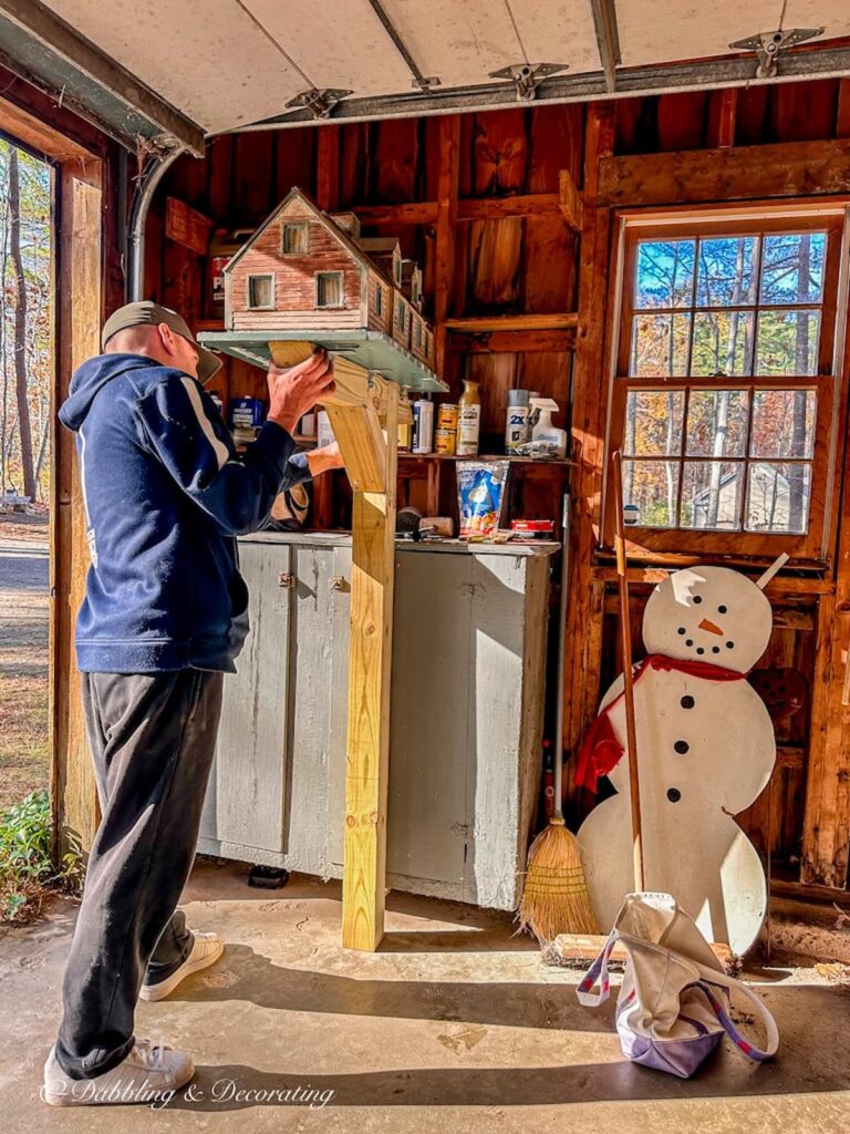 Man holding a unique mailbox house on top of a post in garage.