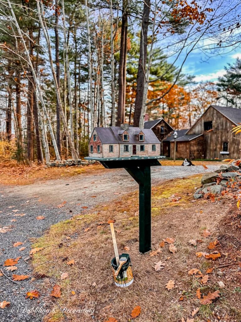 Unique mailbox house on essex green colored post in front of cedar shakes house with paint can.