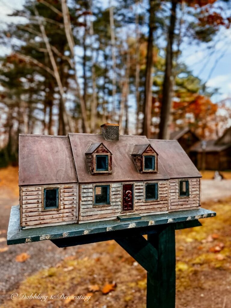 Unique mailbox on post shaped as a rustic house with the number 3 on its door.