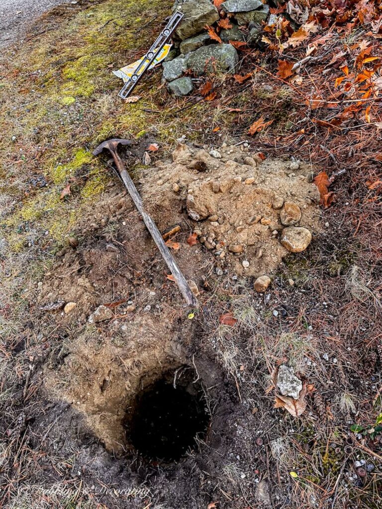 Hole with shovel, level, and cement bag on ground.