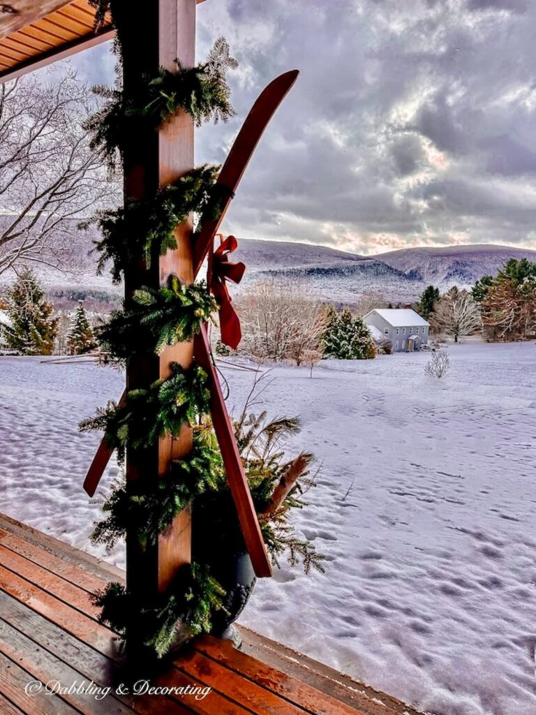 Snowy mountain landscape scenery off front porch with with garland wrapped beam with vintage skis crossed.