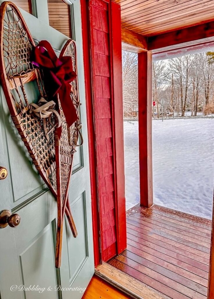 Pair of vintage wooden snowshoes criss crossed on blue front door on red house with burgundy bow.