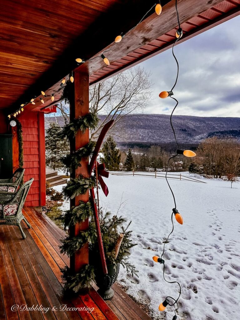 Vintage Christmas lights hanging from porch in snow scene.