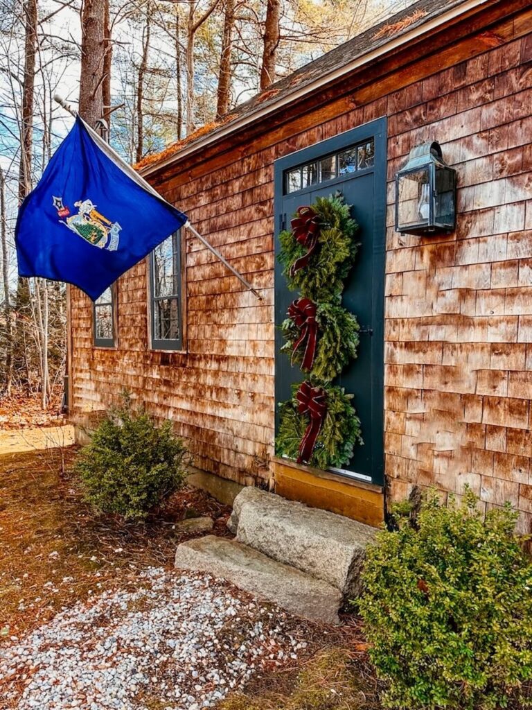 Three Christmas wreaths hanging on 1930s front door with blue Maine flag flying.