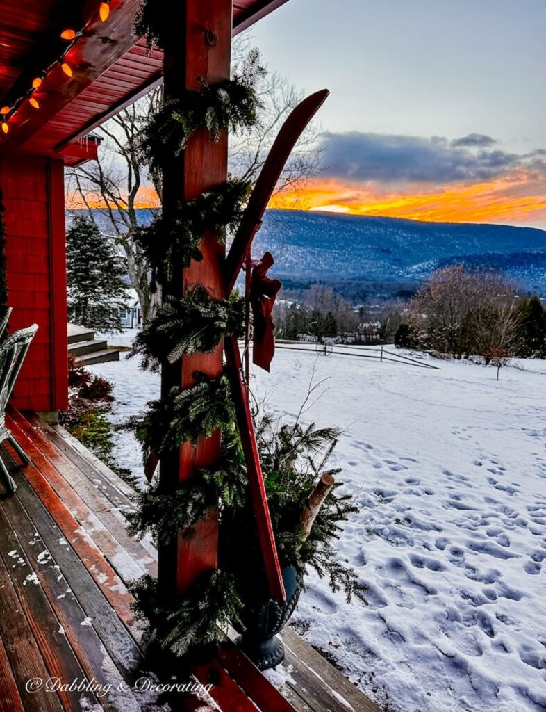 Vintage Christmas skis criss crossed on porch beam looking out to a sunrise in the mountains.