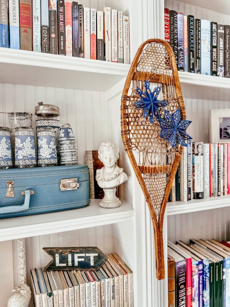 Vintage wooden snowshoe with blue paper star snowflakes hanging on fireside built-ins for a vintage Christmas.